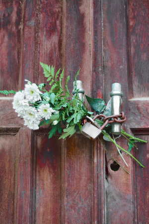 Faded red wooden door closed with a padlock and some flowers.の写真素材
