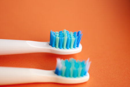 Close-up of two white toothbrushes with blue bristles, one new and the other worn and used on an orange background.の写真素材