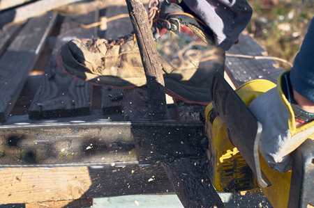 Worker cutting wood outdoors with chainsaw, focused and efficient.