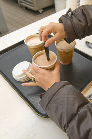 In a cozy coffee shop, a hand holds a tray with three cups of coffee to go, capturing the essence of...