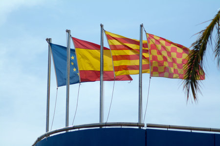 European, Spanish, Catalan and Tarragona flags flutter in the wind on a blue structure under a...