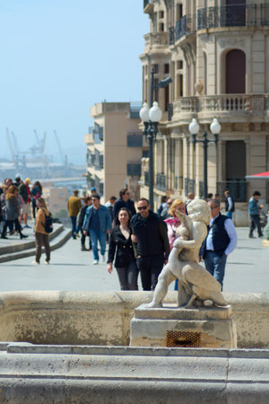 Tarragona, Spain - April 11, 2024: A captivating stone sculpture of two intertwined figures, with the backdrop of a lively boardwalk and lush vegetation, evoking a sense of eternal connection.のeditorial素材