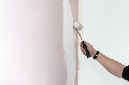 A hand holds a roller applying pink paint to a white wall, symbolizing renewal and transformation.の写真素材