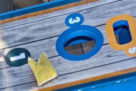 Vibrant blue cornhole game board with detailed scoring zones, striped beanbag beneath, on sunny...