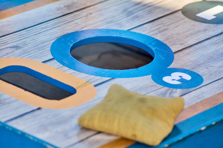 Cornhole game board with scoring zones and striped beanbag, displayed on a patio with wooden...
