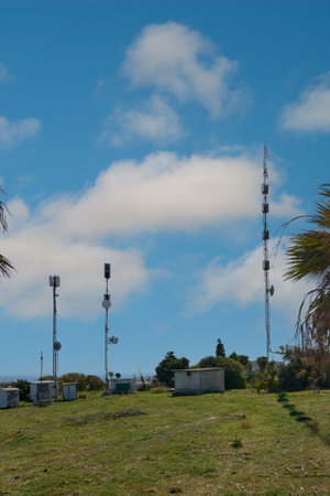 A cluster of telecommunication towers stands in a green landscape in Rhodes, Greece, under a blue...