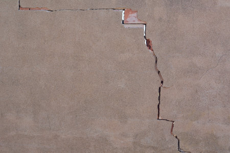 A close-up of a deep crack in a plaster wall. The damage reveals the red bricks underneath, symbolizing wear, decay and the need for repair.の写真素材
