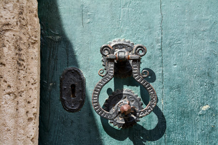 An antique wrought iron knocker and lock on an old door with cracked paint. Concept of security, history, or a secret waiting to be unlocked.の写真素材