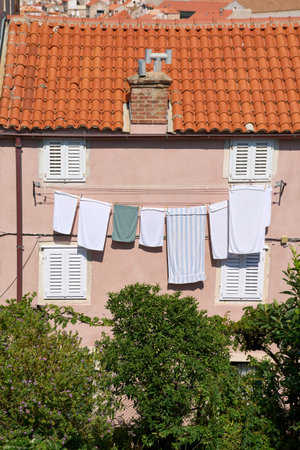 Towels and household laundry drying on a clothesline against a pink Mediterranean-style building facade. Four windows with white shutters frame the domestic scene.の写真素材