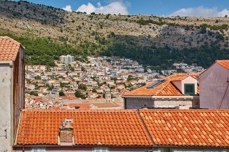 A view over the iconic terracotta rooftops of Dubrovnik, Croatia. In the background, modern houses cover the slopes of Mount Srd under a blue summer sky.の写真素材