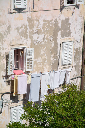 Towels and clothes hang from a clothesline on the weathered stucco wall of an old building. A window with white shutters is open, showing daily life.の写真素材