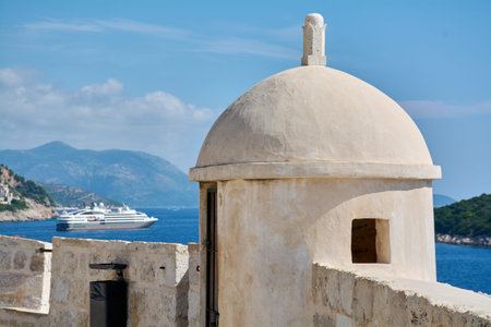 View from the medieval fortress in Dubrovnik on a sunny day. An ancient stone sentry box contrasts with a modern cruise ship at a popular tourist destination.の写真素材