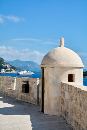 Detail of a watchtower turret on the Dubrovnik city walls. A large cruise ship sails on the Adriatic Sea in the background, near the coast of Croatia.の写真素材