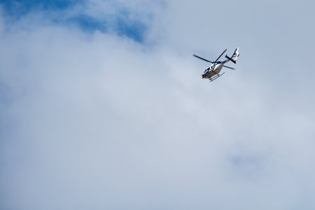 A white and blue emergency services helicopter flies on a rescue or surveillance mission. The aircraft is in flight against a blue sky with white clouds.の写真素材