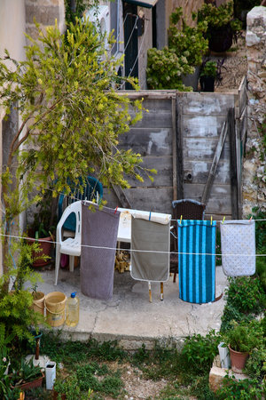 Colorful towels and laundry drying on a clothesline in a rustic courtyard. Real life scene in a Mediterranean garden with plants and a wooden gate.の写真素材