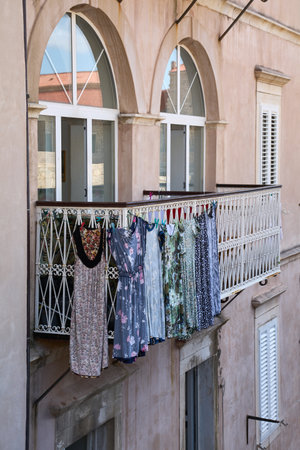 Colorful summer dresses and clothes drying on a clothesline on a balcony in Dubrovnik, Croatia. The laundry hangs from an ornate metal railing on a historic building.の写真素材