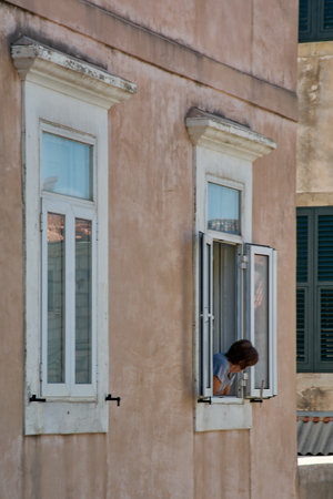 A woman leans out of an open window in Dubrovnik's Old Town. Authentic local life scene in a historic building on the Adriatic coast.の写真素材