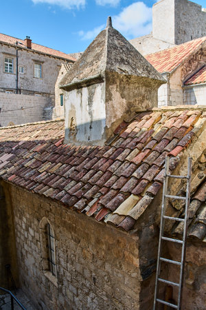A view from the city walls of Dubrovnik showing weathered terracotta tile rooftops, an old stone chimney, and a ladder.の写真素材