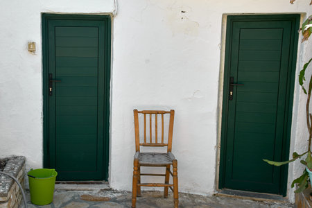 Rustic wooden chair between two green doors on white wallの写真素材