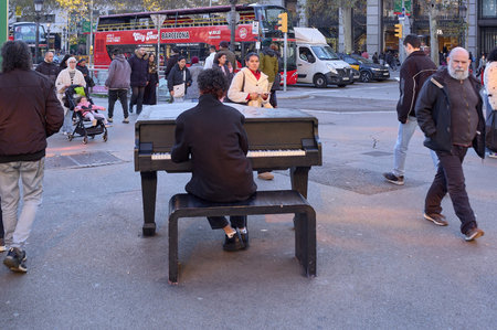 Barcelona. Spain - January 10, 2026: A pianist from behind plays a grand piano on a busy street with...