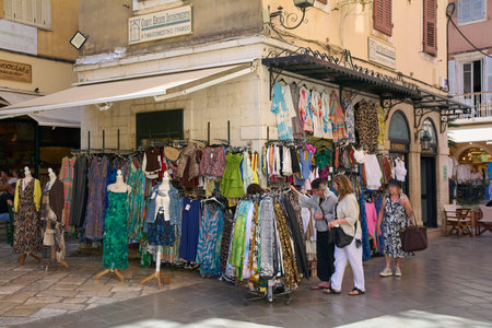 Corfu. Greece - January 29, 2026: Tourists browse colorful dresses and garments displayed outside a boutique, reflecting summer travel culture, local retail activity, and relaxed shopping in a historic Mediterranean setting.のeditorial素材