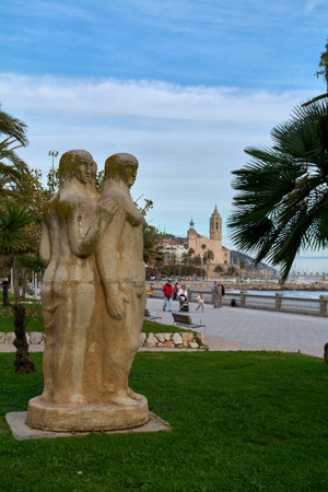 Sitges. Spain - February 12, 2026: Tres mujeres sculpture on the seafront promenade with church and Mediterranean coastline, iconic cultural landmark and travel attraction in Cataloniaのeditorial素材