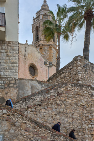 Sitges. Spain - February 17, 2026: Mediterranean religious landmark with weathered masonry, circular window and coastal fortification textures in seaside setting.のeditorial素材