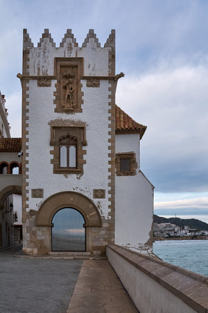 Sitges. Spain - February 18, 2026: Historic tower facade of maricel palace overlooking the mediterranean waterfront in sitges, featuring gothic arch, stone details and coastal promenade under cloudy skyのeditorial素材