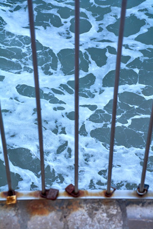 Love locks secured to seaside barrier overlooking turbulent sea water along urban waterfront in coastal Catalonia.の写真素材