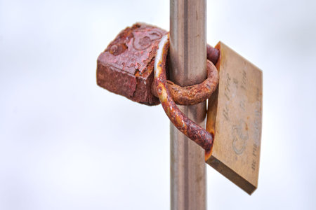 Aged security lock with peeling paint and heavy rust detail secured around steel railing,...