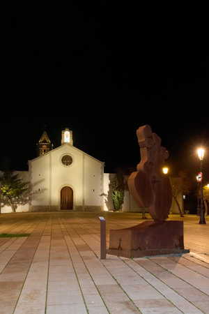 Sitges. Spain - March 05, 2026: Night view of Mujer mirando al mar public sculpture by Horacio Elena with Ermita de Sant Sebastia chapel facade and urban square near Mediterranean coast.のeditorial素材