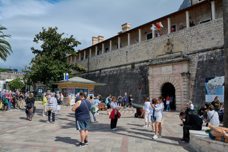 Kotor. Montenegro - March 20, 2026: Tourists gather at the Sea Gate entrance to the medieval old town fortifications with historic cannons and a tourist information kiosk in the harbor plaza.のeditorial素材