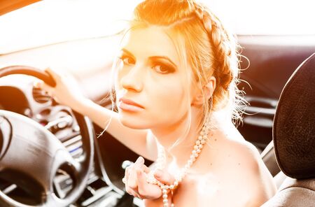 Young Woman in a pearl necklace sat In the drivers seat of her carの写真素材