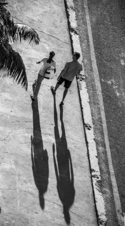 Silhouette of a man and a woman casting long shadows on a concrete roadの写真素材