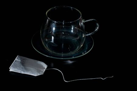 teabag by an empty glass cup  isolated on blackの写真素材