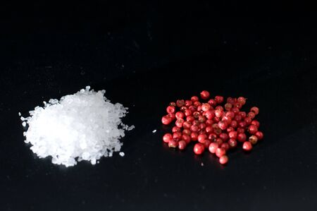 coarse salt and red pepper corns scattered on black backgroundの写真素材