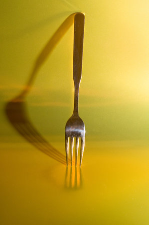 single fork positioned vertically with its shadow behind against colourful background