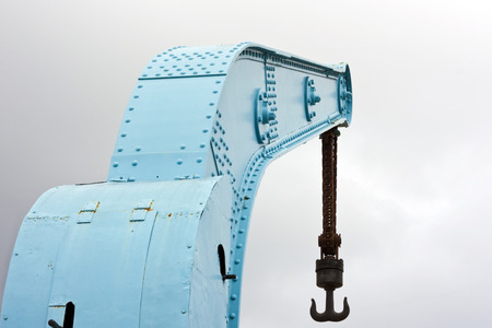 Old blue crane with rusty chain and hook on harbor with cloudy skyの写真素材