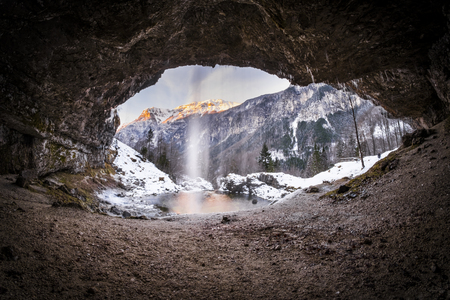 View from a cave to waterfall Goriuda and sun shines on mountains in Italian alpsの写真素材