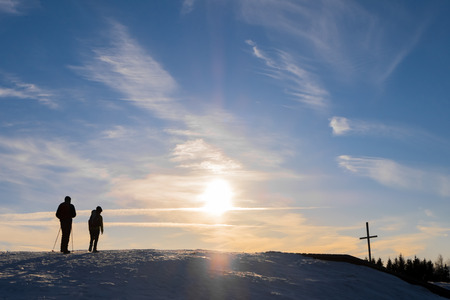 Father and son hiking on snowy mountain Schoeckl to summit cross with nice sunset in Austriaの写真素材