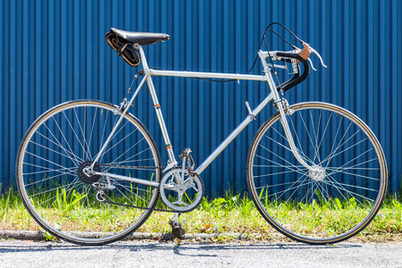 Vintage racing bicycle from the 60s with chrome steel frame in front of blue wall and green grassの写真素材