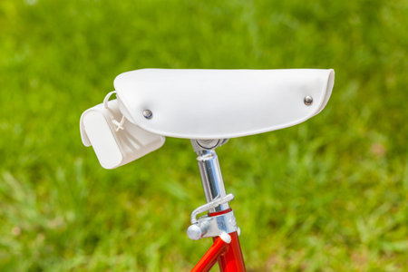 White saddle with saddlebag on red vintage classic 1970s folding bike with brurred green grass in backgroundの写真素材