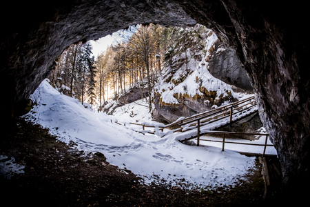 View from dark cave to snow covered gorge Baerenschuetzklamm with forest and wooden bridge in winterの写真素材
