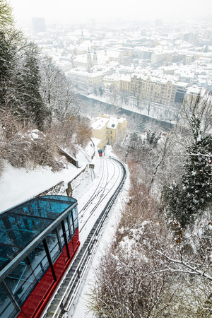 Red funicular railway cable car on hill Schlossberg with aerial view to snow covered city Graz in winterの写真素材