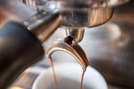 Fresh espresso dripping from portafilter of coffee machine into white cupの写真素材