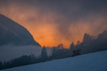 Dramatic sunset behind the forest near mountain Grimming on a very foggy evening on a winterday in Styria, Austriaの写真素材
