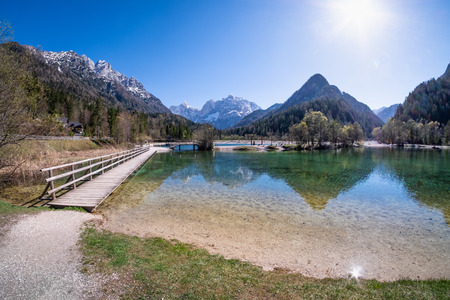 Bridge over lake Jasna with mountains Razor and Prisojnik on the horizont in Sloveniaの写真素材