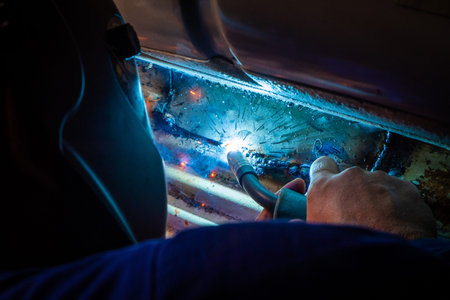 Man with a helmet and no gloves welds in the metal of a car and repairs a rusty holeの写真素材