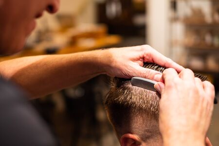 Barber shaves the parting of a young man's hair with a razor blade in his barbershopの写真素材