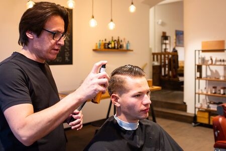 Barber moistens the hair of a young man with a spray bottle in his barbershop, ready for a haircutの写真素材